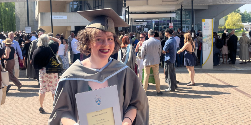 Mary is wearing a degree cap and gown, while holding a degree certificate